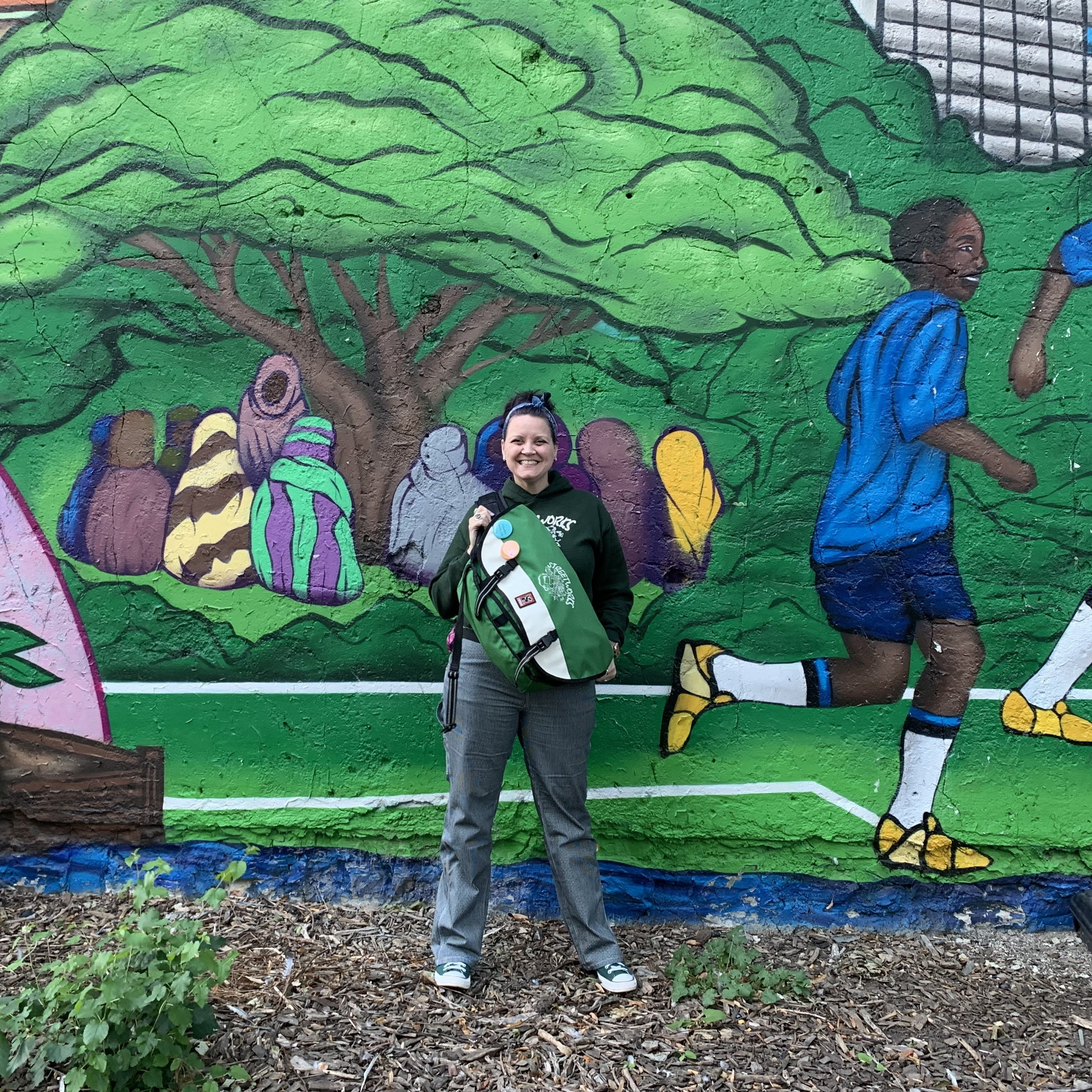 Photo of Natasha standing in front of a mural holding a GreenBag